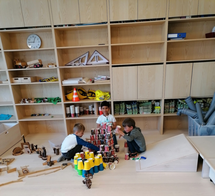 Drei Jungs bauen einen Turm aus vielen Bechern.