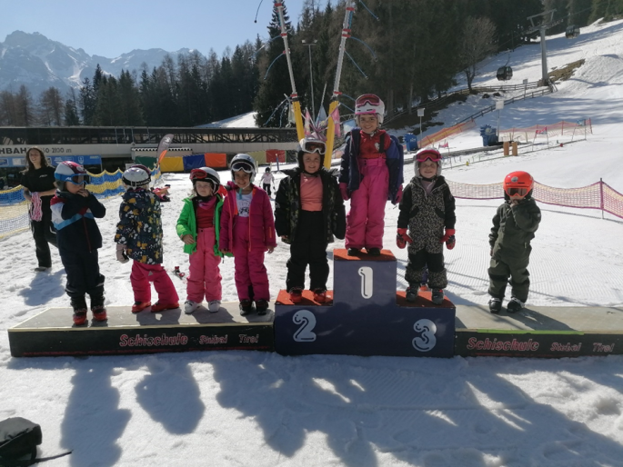 Preisverleihung bei der Mittelstation der Schlick 2000 von der Schischule Stubai, 8 Kinder mit Skianzug, drei davon am Podium, alle lächeln, der Himmel ist blau
