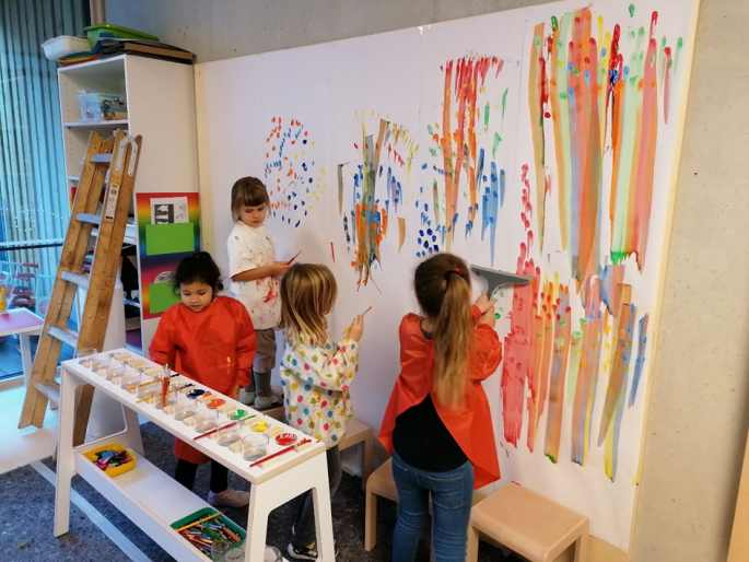 vier Kindergartenkinder malen mit Wasserfarben auf eine große Leinwand  