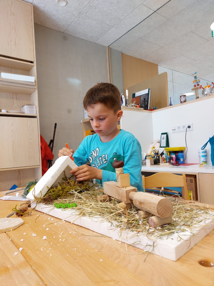 Ein Junge stellt ein kreatives Kunstwerk auf einem Tisch aus Styropor, Holzspäne und Holzklötze her.