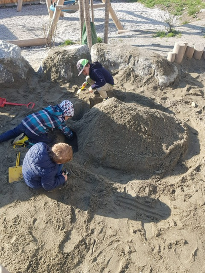 Drei Jungs bauen eine riesengroße Sandburg mit Wassergraben im Freien.